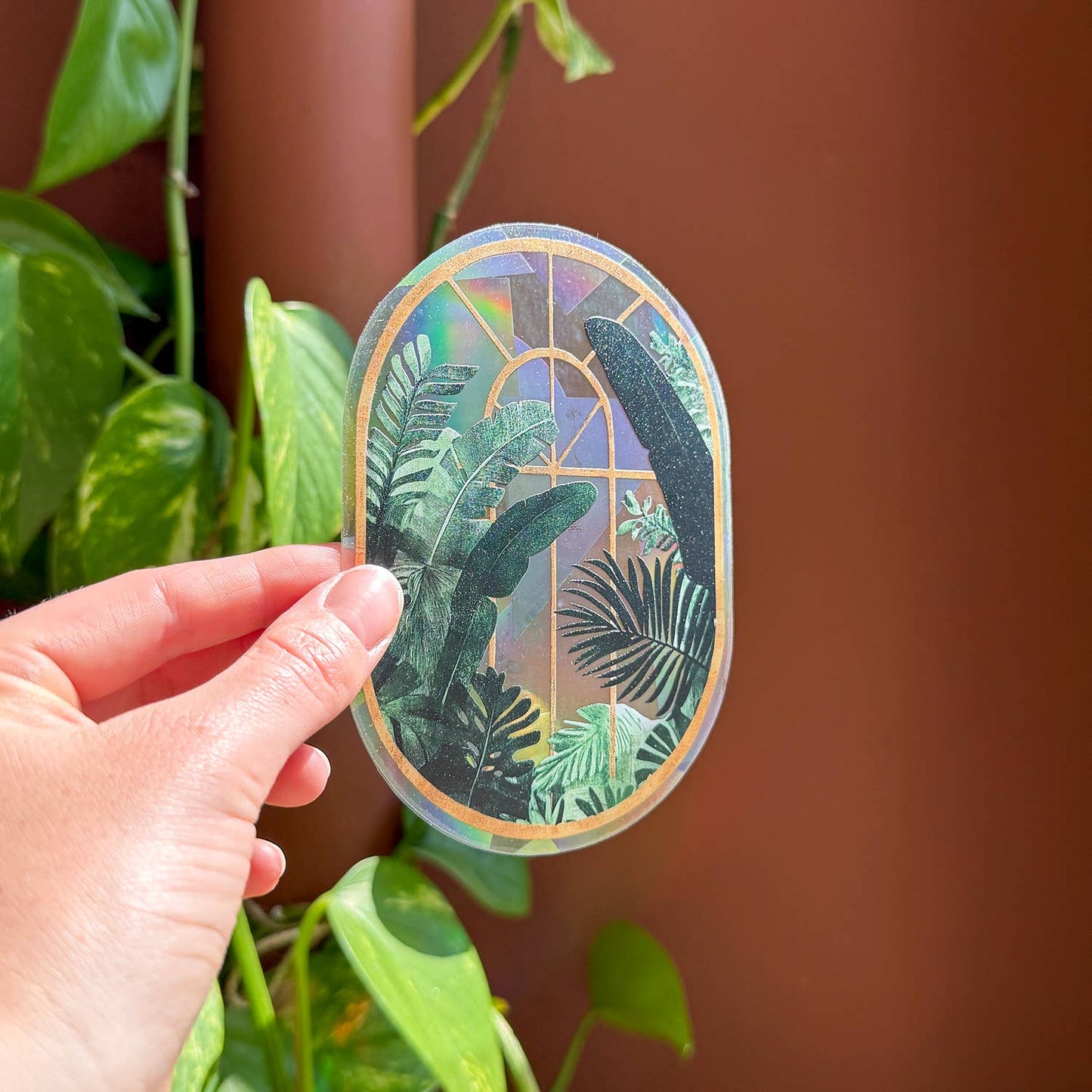 Hand holding a decorative sticker with plant-themed design against a brown background