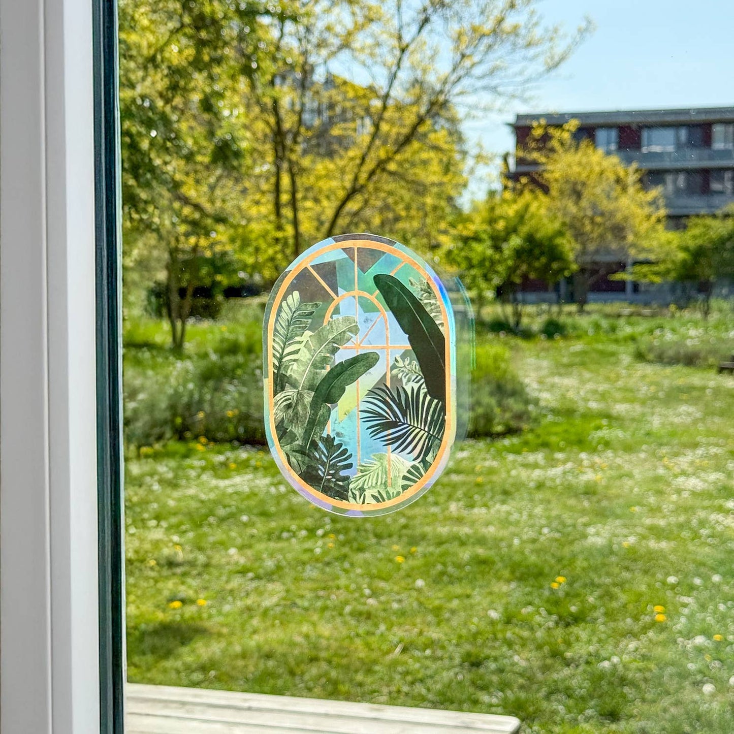 Decorative window sticker with leaf design on a glass pane, showing a view of a garden and building.