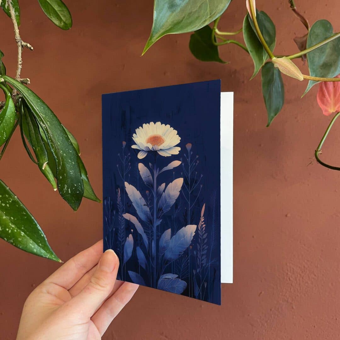 Hand holding a blue card with floral design against a brown background