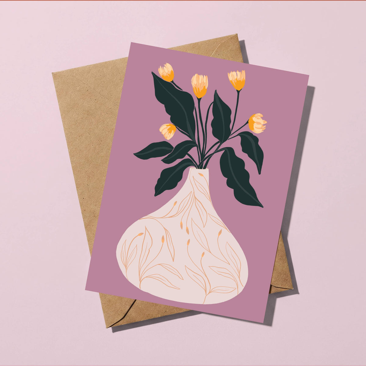 A square greeting card with an illustration of yellow tulips in a cream vase against a dusty purple background, shown with a brown kraft envelope on a light pink surface.
