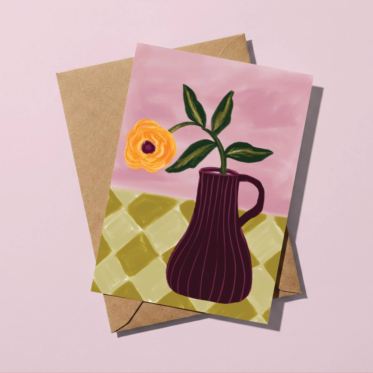 A square greeting card with a watercolor-style illustration of a yellow-orange flower in a dark purple vase, placed on top of a kraft paper envelope against a soft pink background.