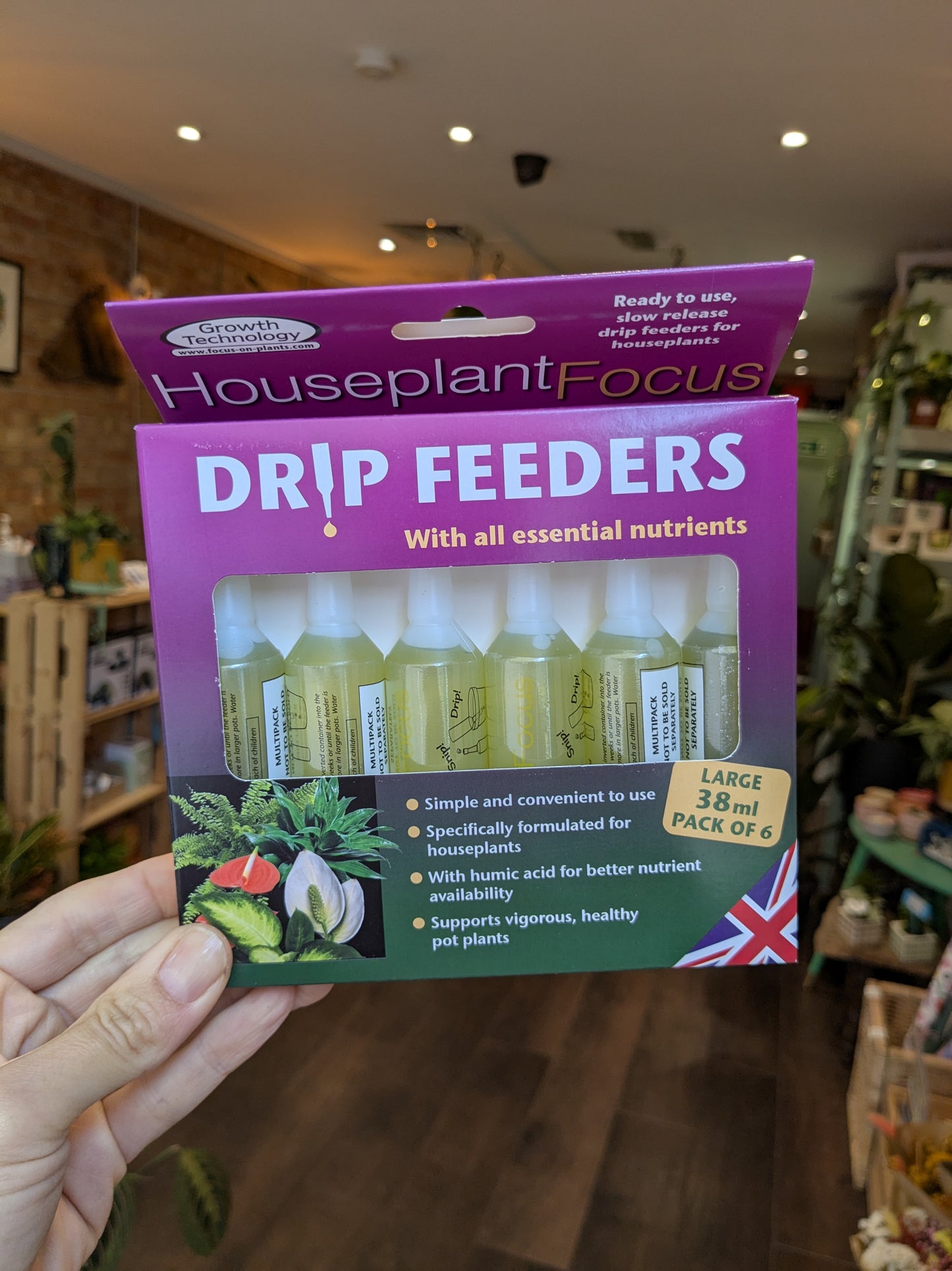 Packaging of Houseplant Focus Drip Feeders held in a hand with a store interior background.