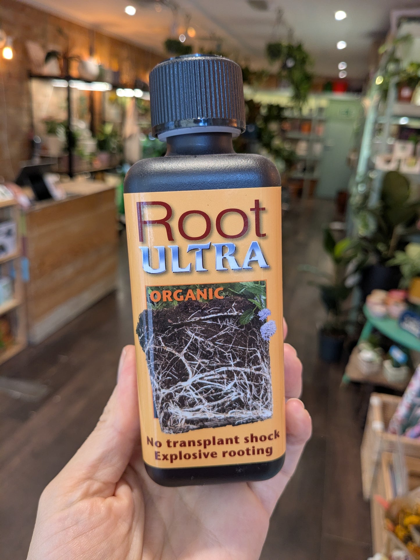 Bottle of Root Ultra Organic plant growth supplement held in a hand with a store interior in the background.
