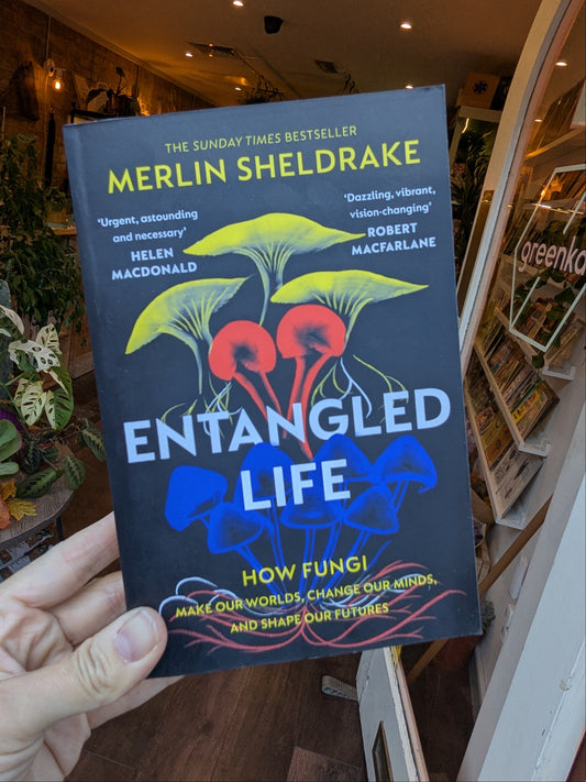 Book titled 'Entangled Life' by Merlin Sheldrake held in a hand with a store interior in the background.