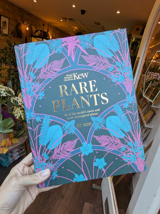 Book titled 'Rare Plants' by Kew held in a hand with a plant store in the background