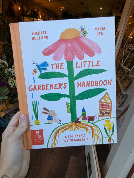 Book titled 'The Little Gardener's Handbook' held by a person indoors.