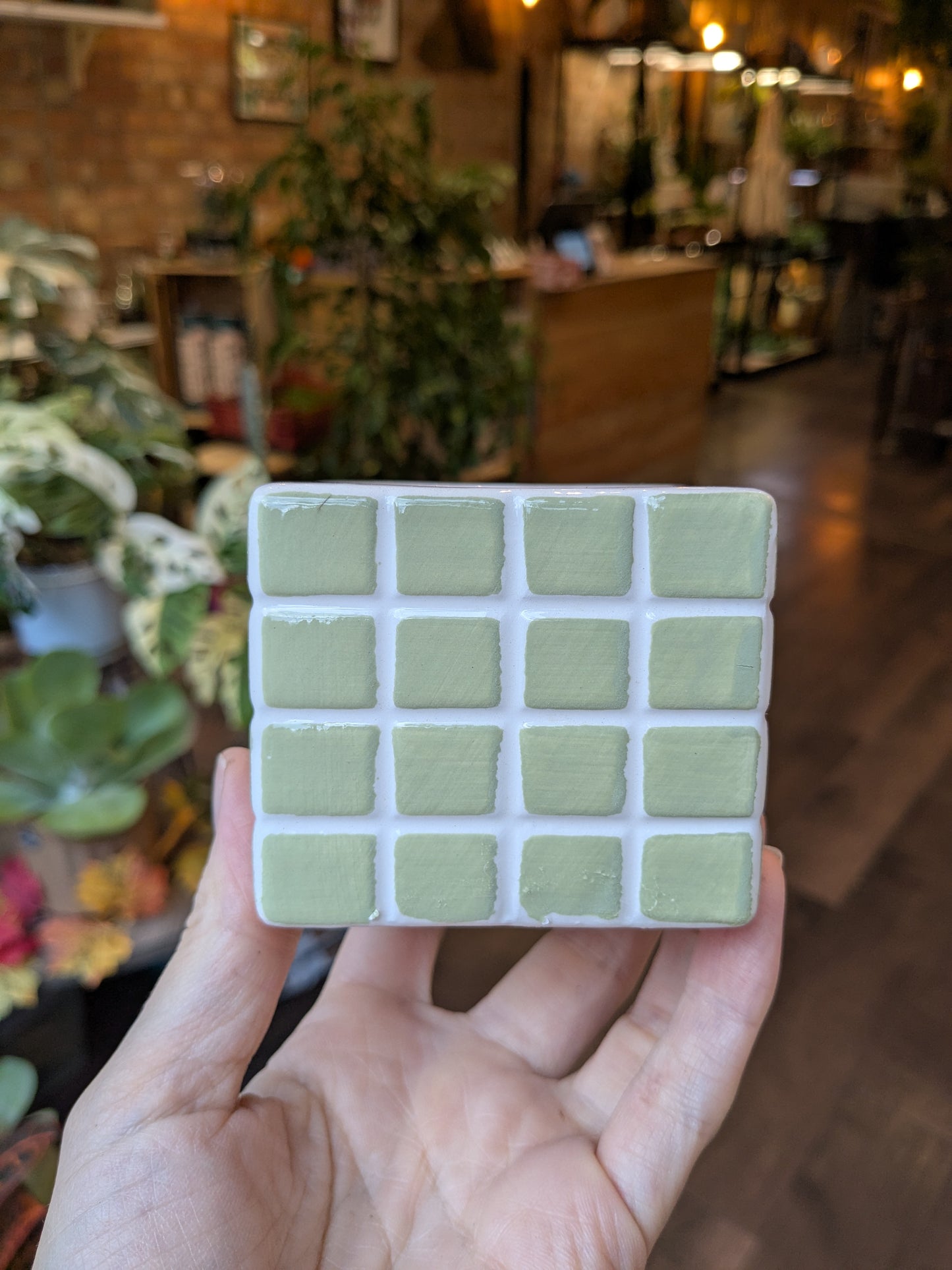 Hand holding a square tile with green squares in a store setting