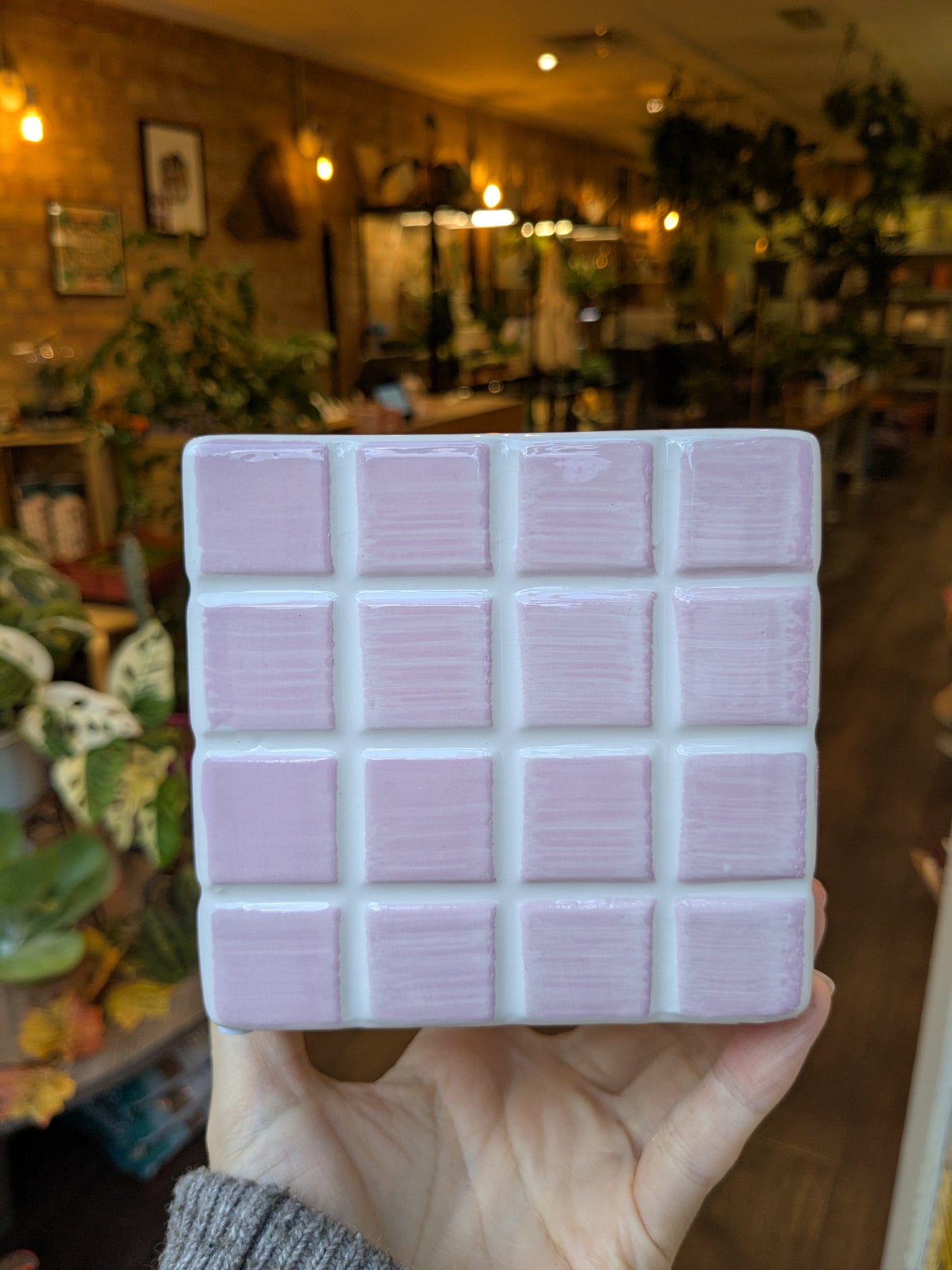 Hand holding a square wax melt container with multiple compartments in a store setting