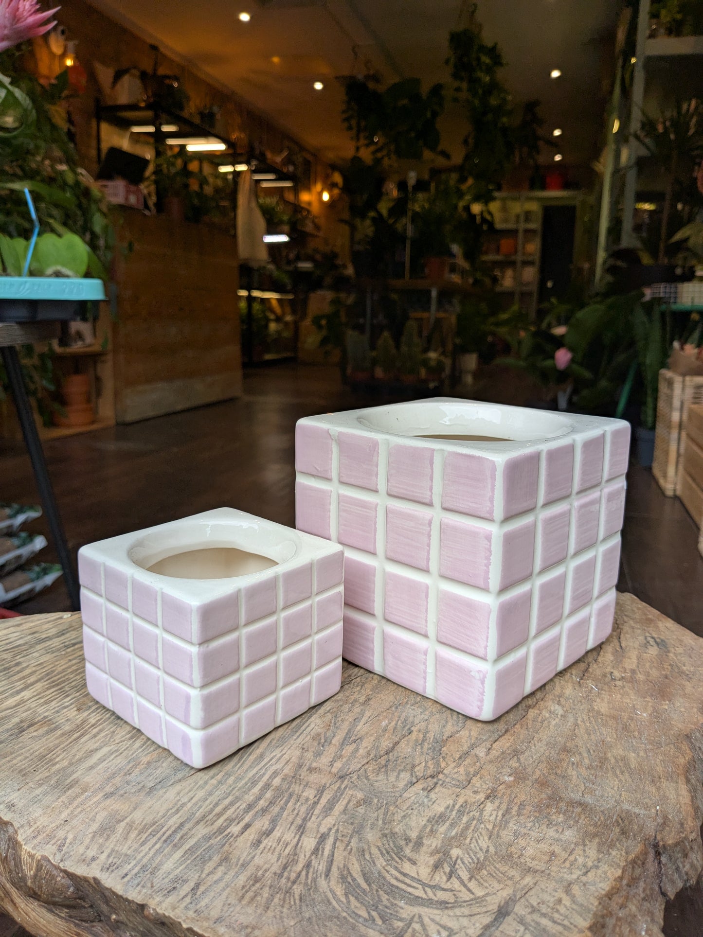 Two square ceramic planters with a grid pattern on a wooden surface in a store setting.
