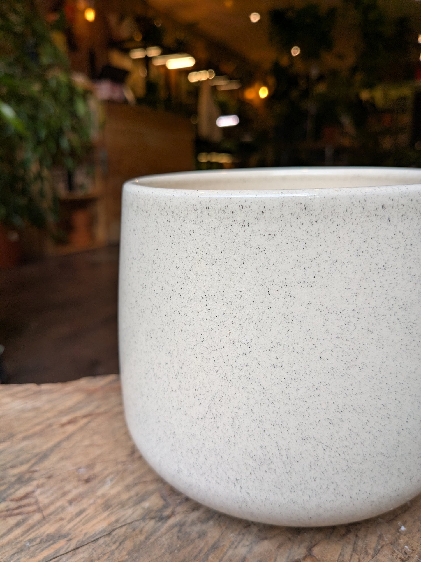 Speckled beige pot on a wooden surface with a blurred indoor background