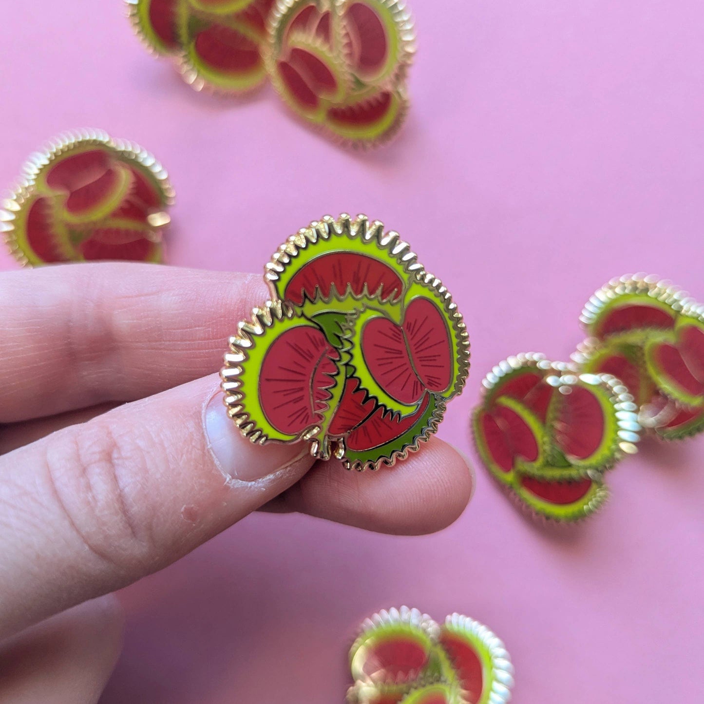 Fruit-themed earrings held by a hand against a pink background