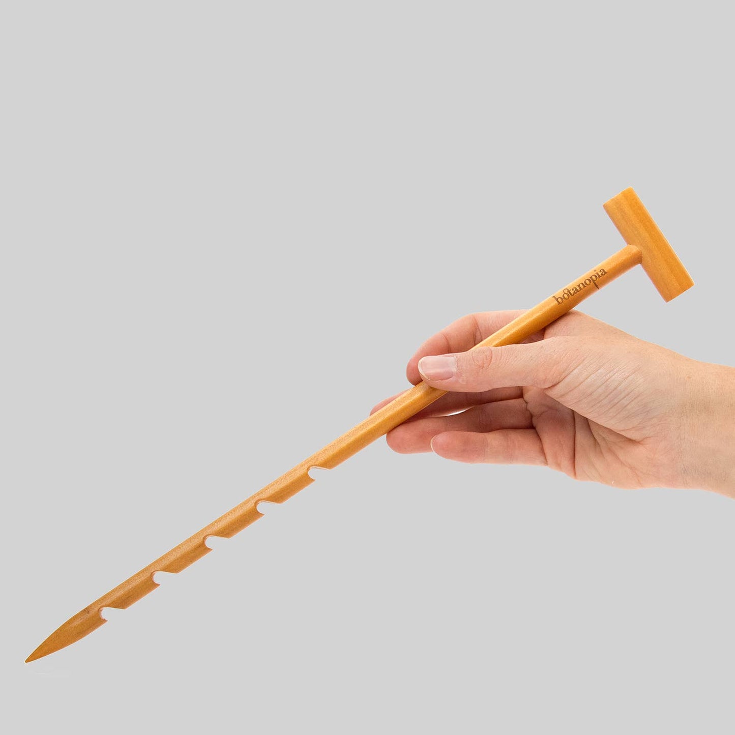 Hand holding a wooden tool against a gray background