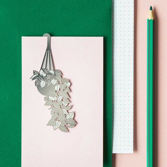 Decorative metal plant wall art on a pink surface with a green pencil.