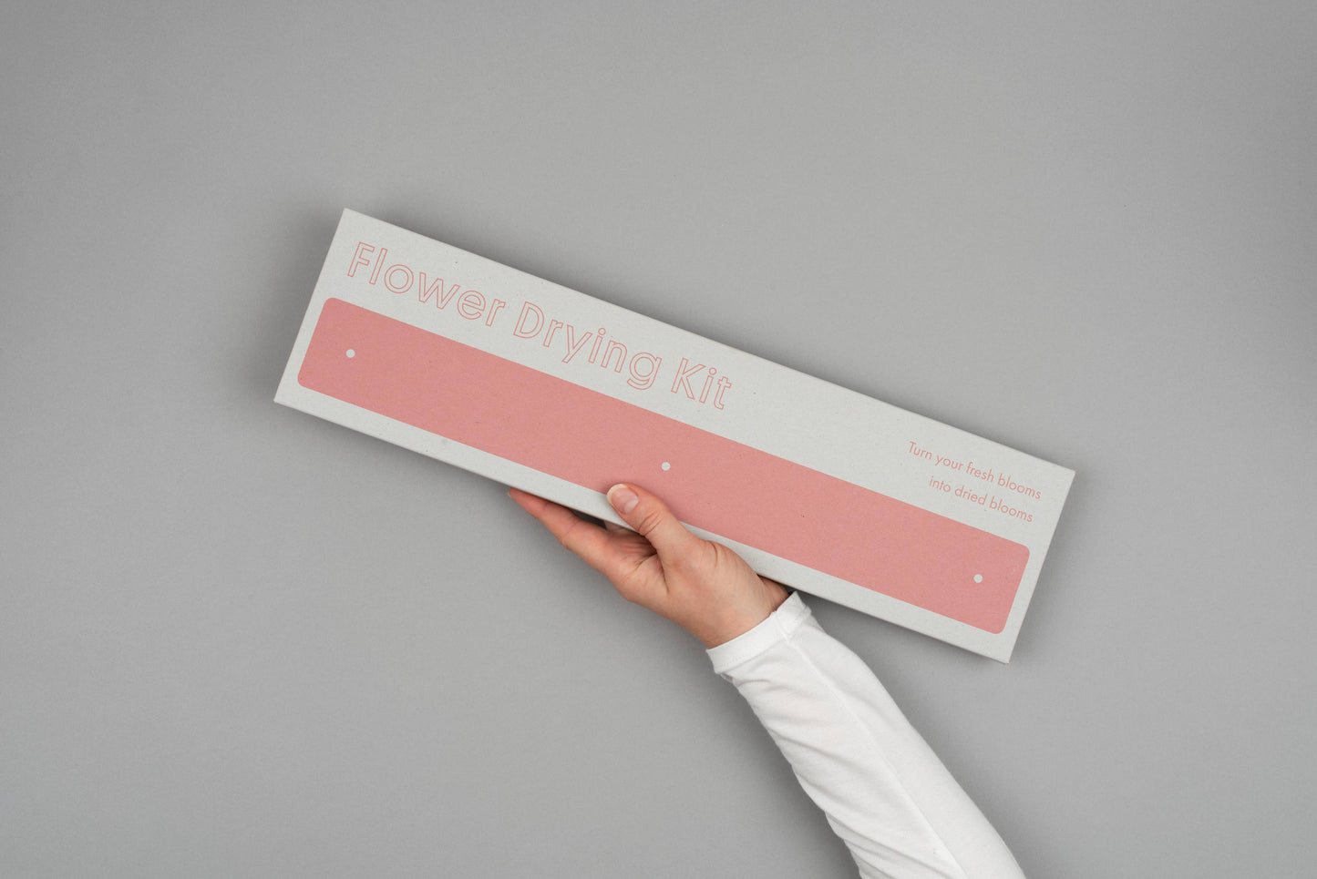 Hand holding a 'Flower Drying Kit' against a gray background