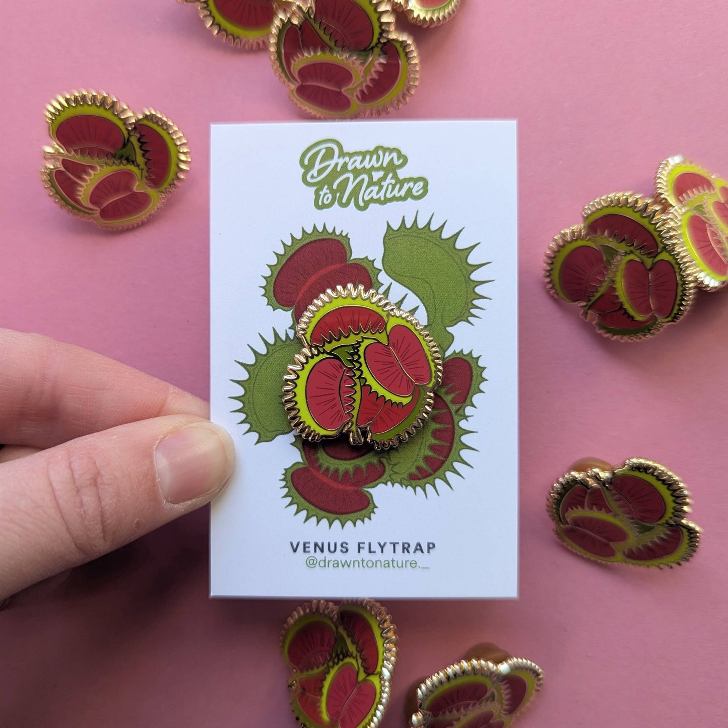 Venus flytrap earrings on a card held by a hand with pink background