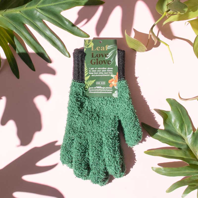 Green gardening glove with a label on a pink background with plant leaves.