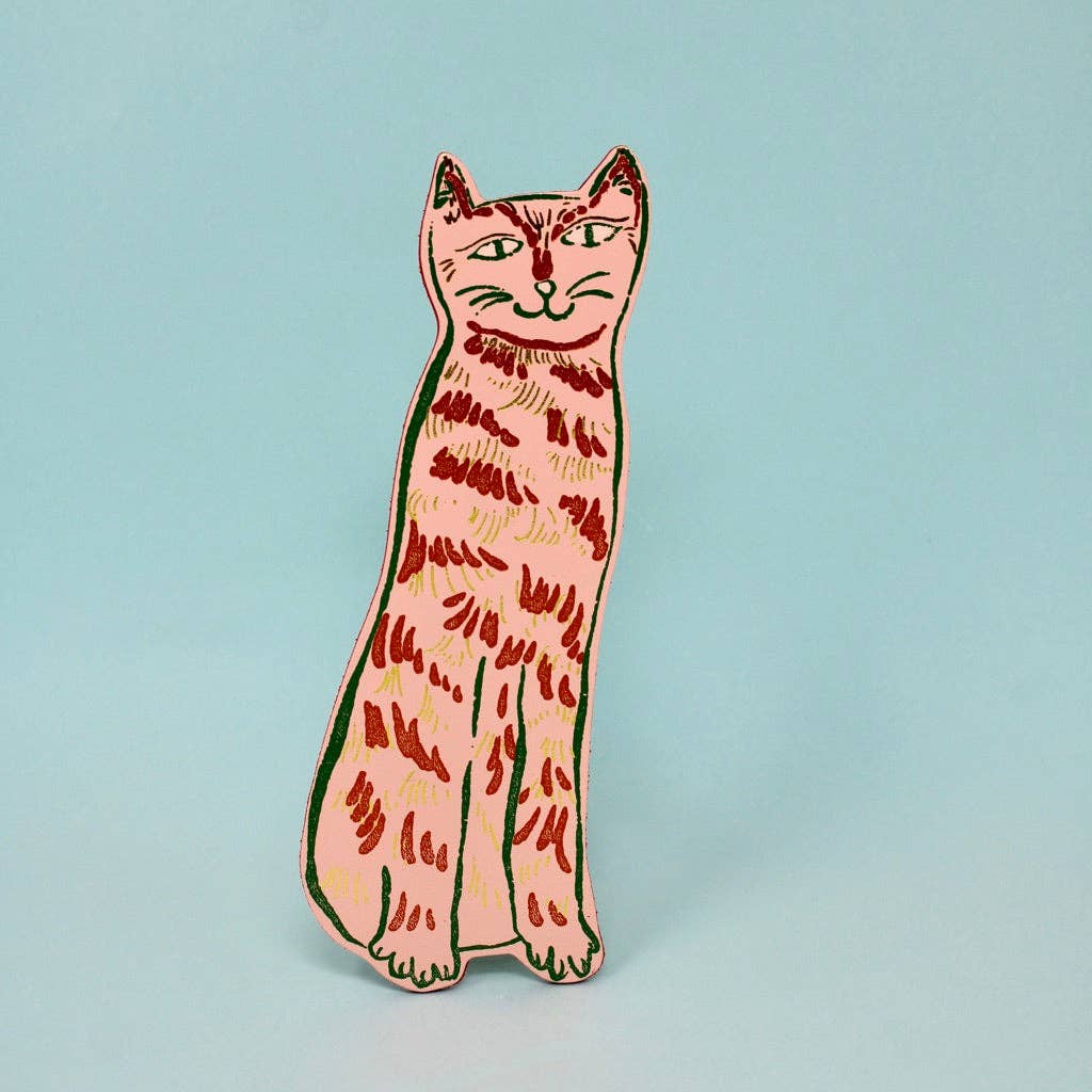 Cat-shaped enamel pin on a light blue background