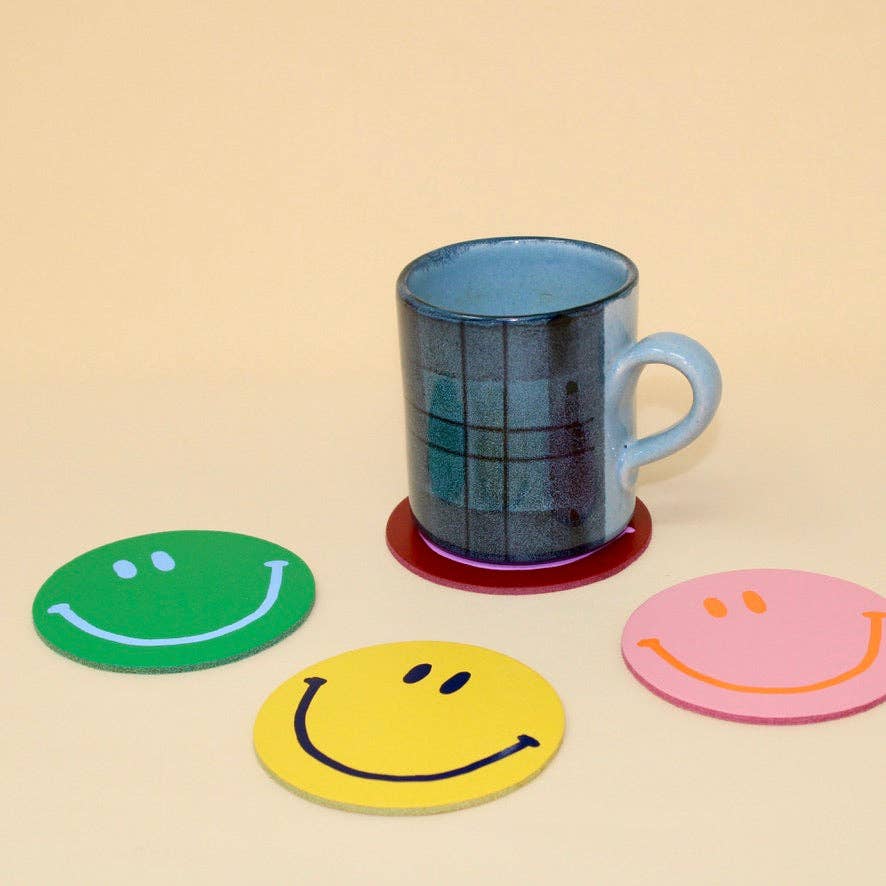 Blue mug on a beige surface with smiley face coasters in green, yellow, and pink.