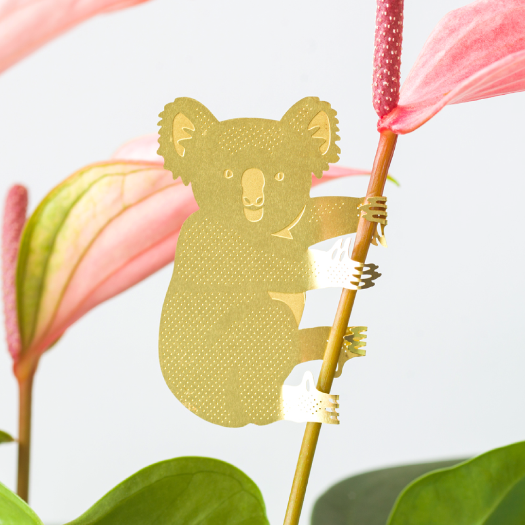 Gold paper cutout of a koala holding pink flowers with green leaves in the background
