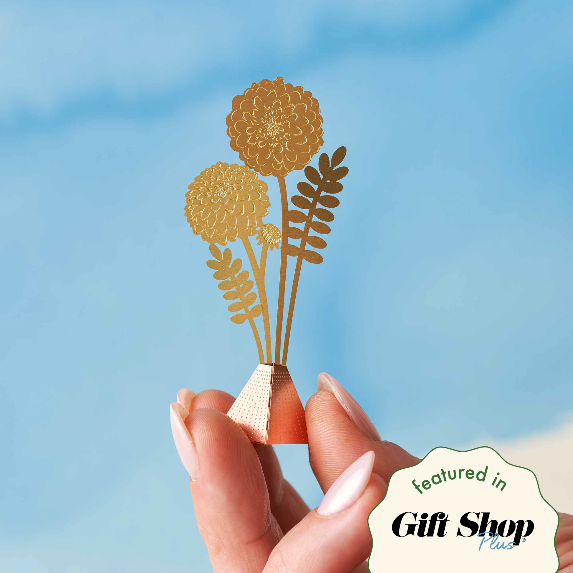 Hand holding a small decorative item with floral design against a blue background