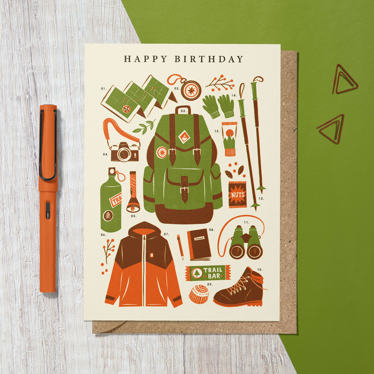 Birthday card with hiking-themed illustrations on a wooden surface with a pen.