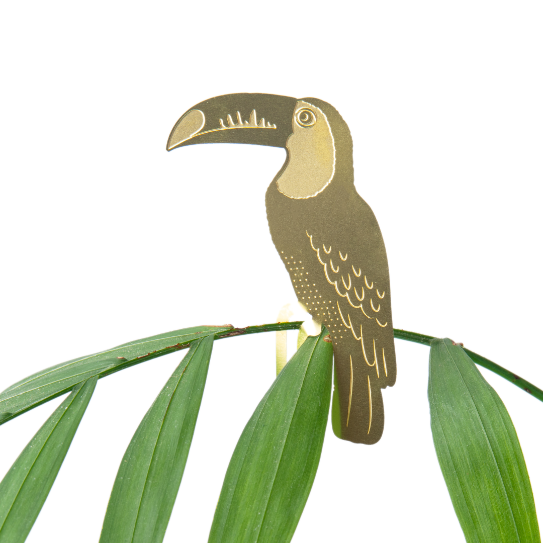 Decorative brass toucan on a branch with green leaves against a white background