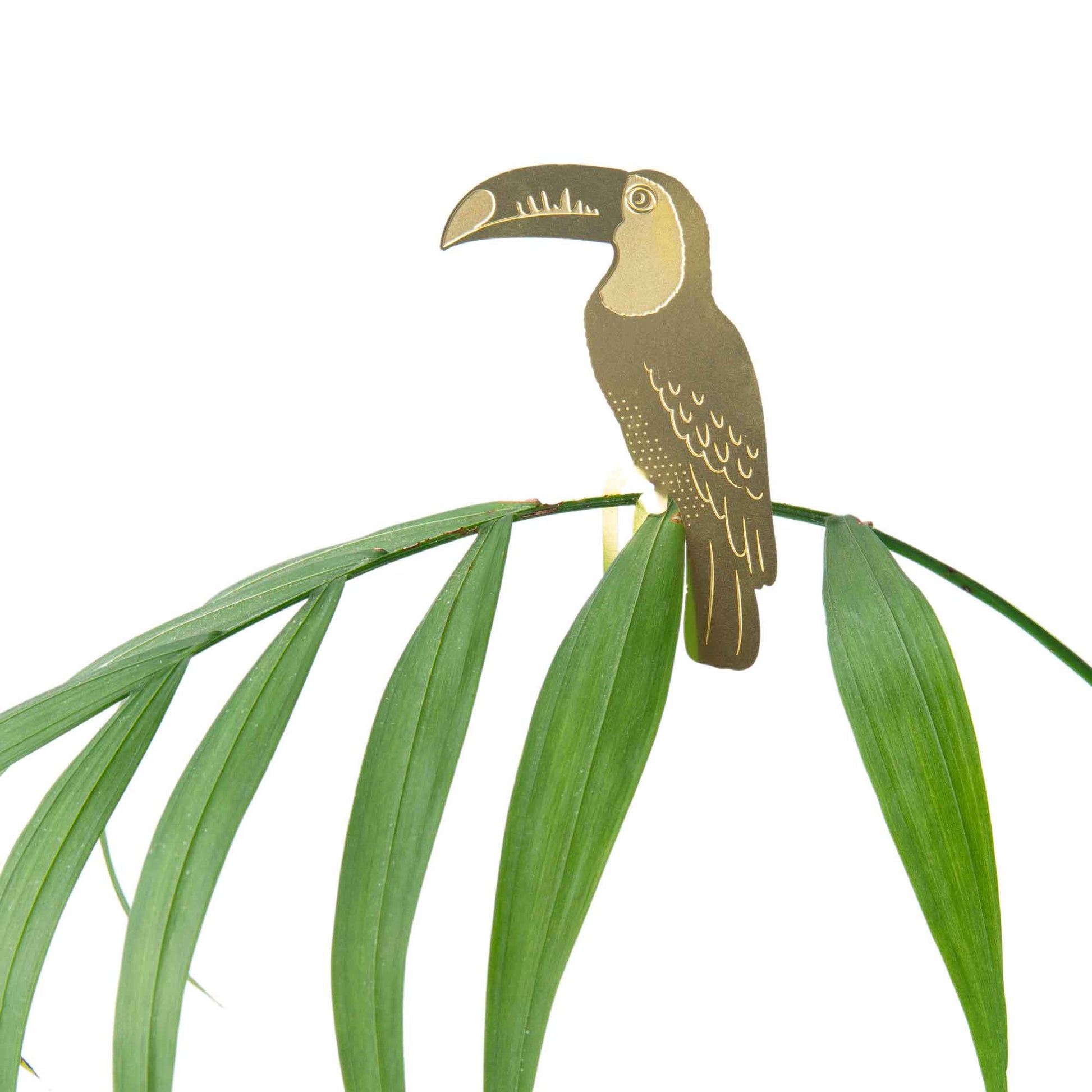 Decorative brass toucan on a branch with green leaves against a white background