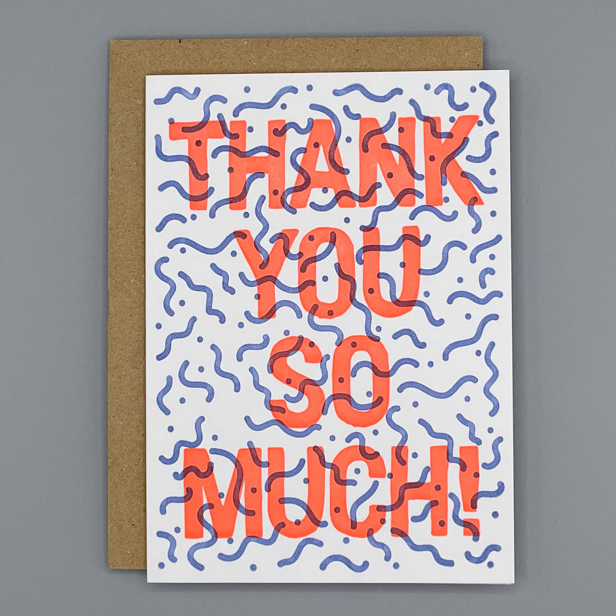 A square greeting card with a kraft envelope, featuring the words 'THANK YOU SO MUCH!' in large coral-red letters over a white background with blue wavy doodle lines.