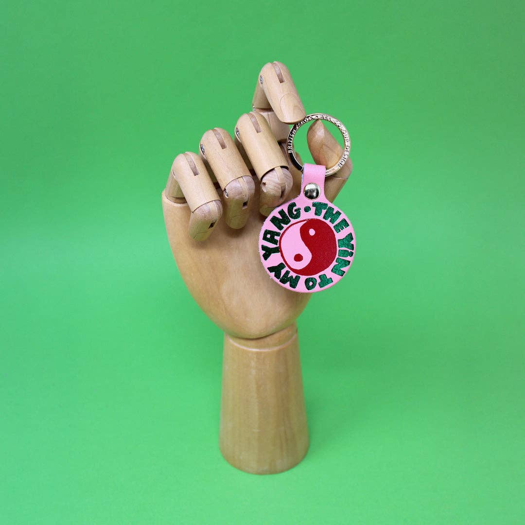 Keychain with yin and yang symbol held by a wooden hand against a green background