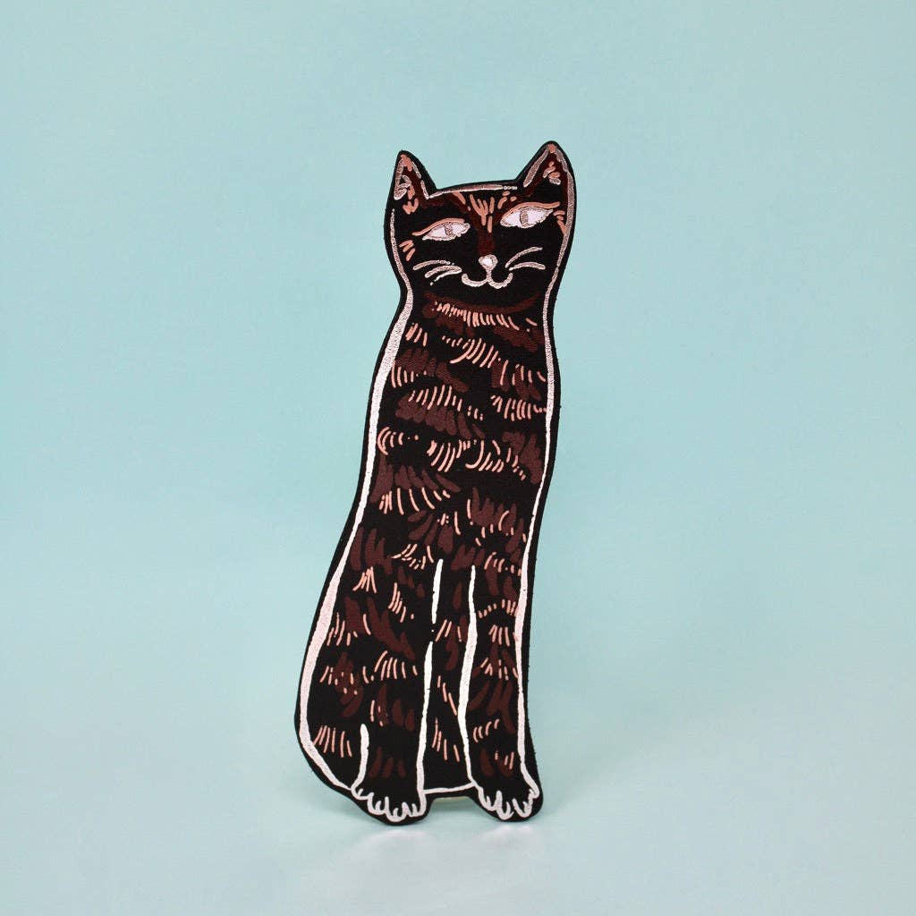 Cat-shaped enamel pin on a light blue background