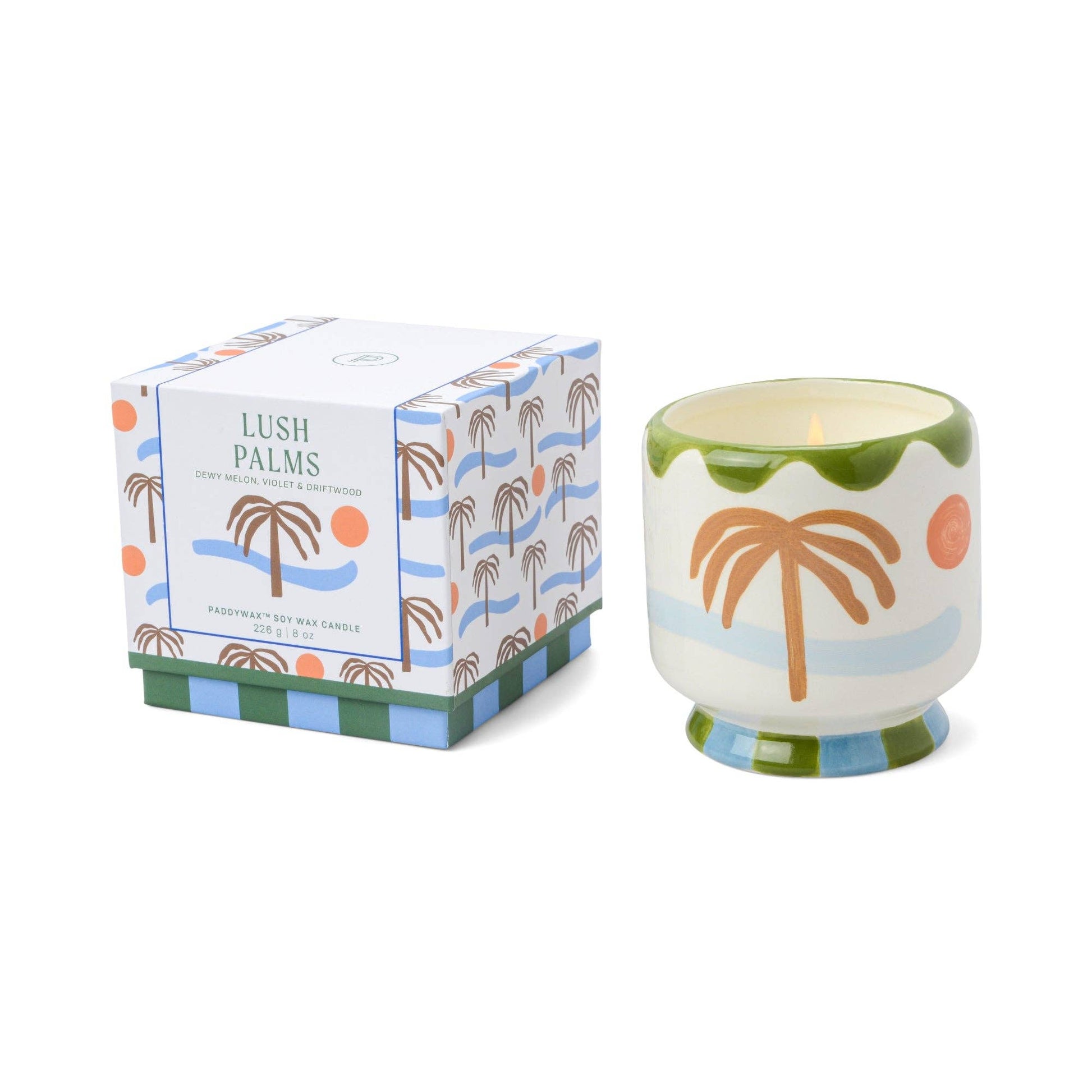Candle with palm tree design next to its packaging on a white background