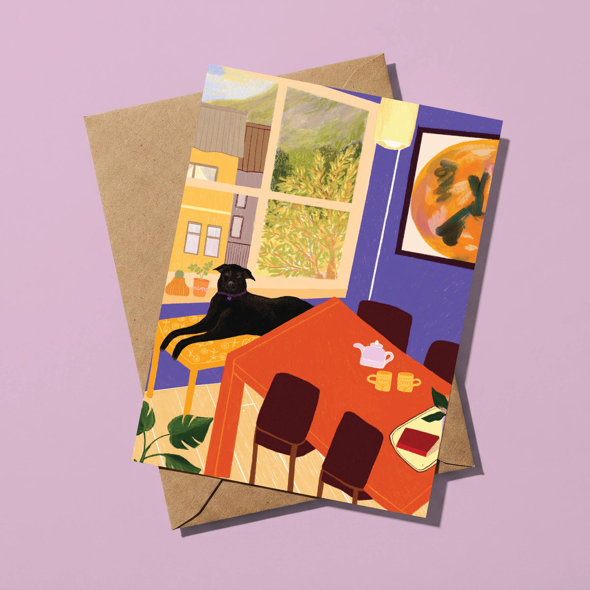 A square art print or greeting card featuring a colorful illustrated dining room scene with a black cat lying by a window, layered over a kraft paper envelope on a lavender background.