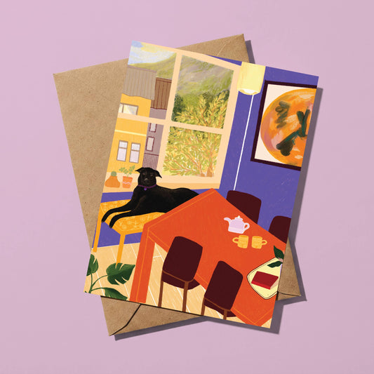 A square art print or greeting card featuring a colorful illustrated dining room scene with a black cat lying by a window, layered over a kraft paper envelope on a lavender background.