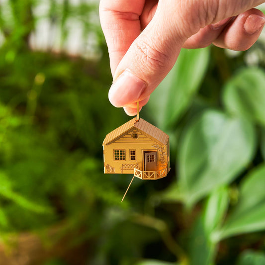 Gold house-shaped pendant held by a hand against a green leafy background