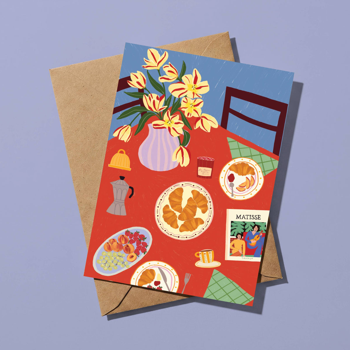 A square illustrated greeting card with a kraft envelope, shown on a soft lavender background. The card features a colorful breakfast table scene with yellow tulips in a vase, plates of food, a coffee pot, and a small 'MATTINE' card.