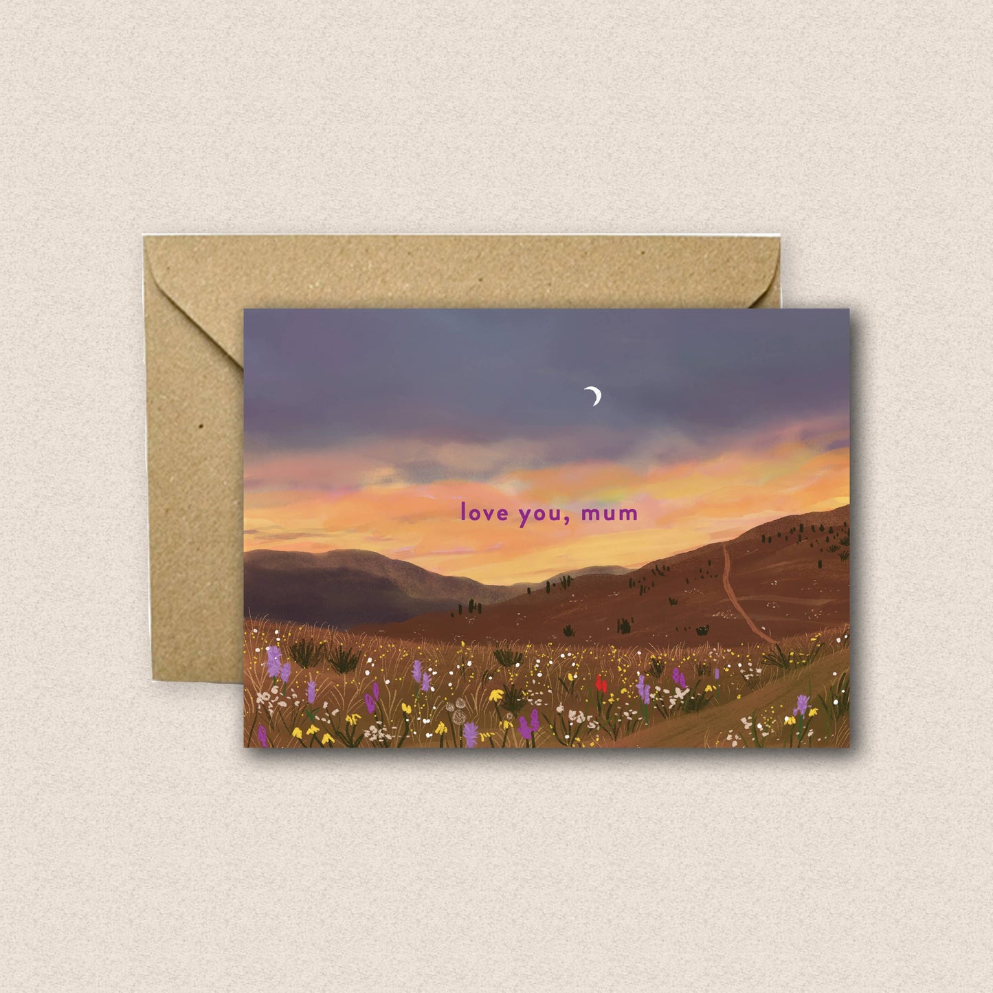Greeting card with sunset landscape and 'love you, mum' text, accompanied by a brown envelope on a beige background.