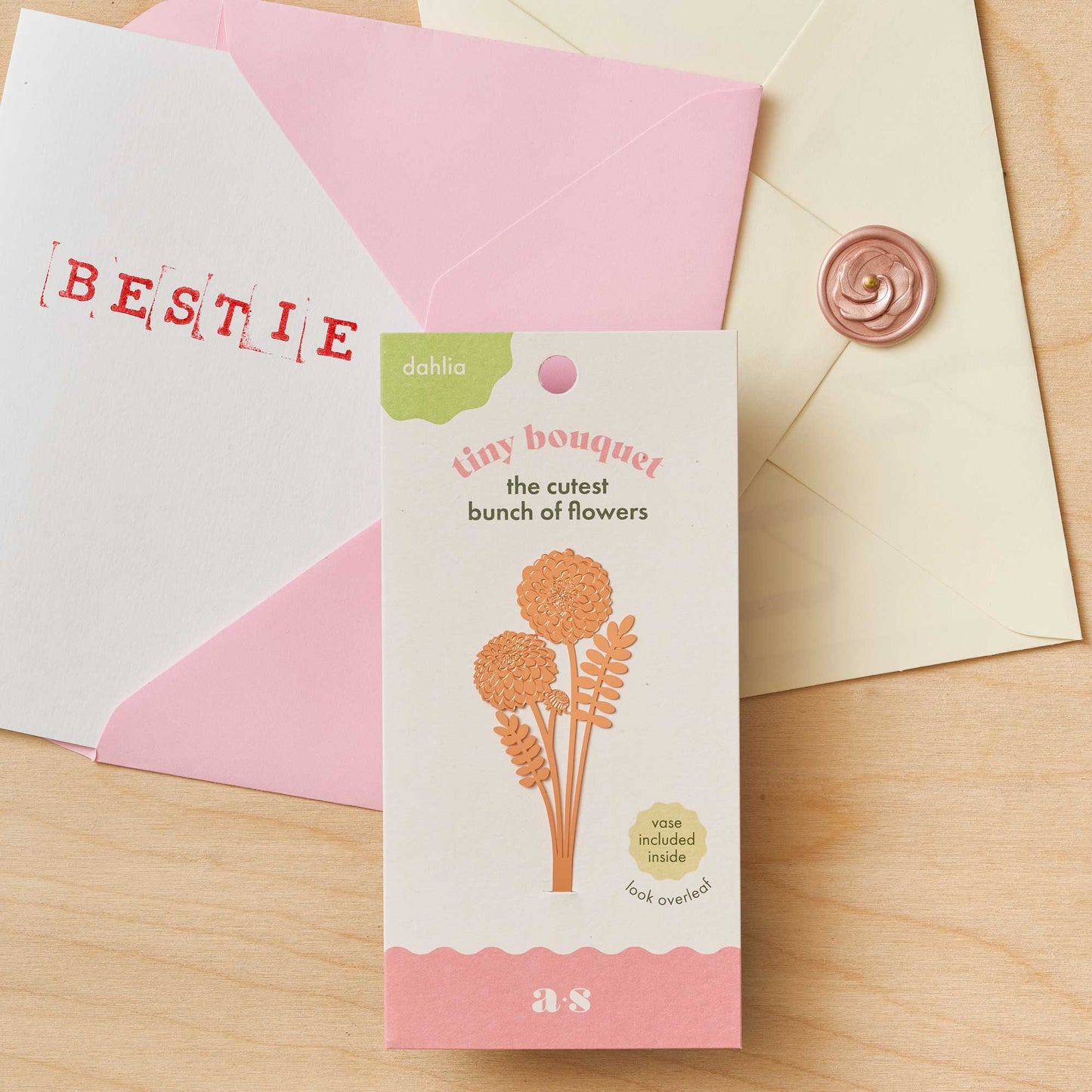 Floral-themed card with 'BESTIE' envelope and decorative elements on a wooden surface