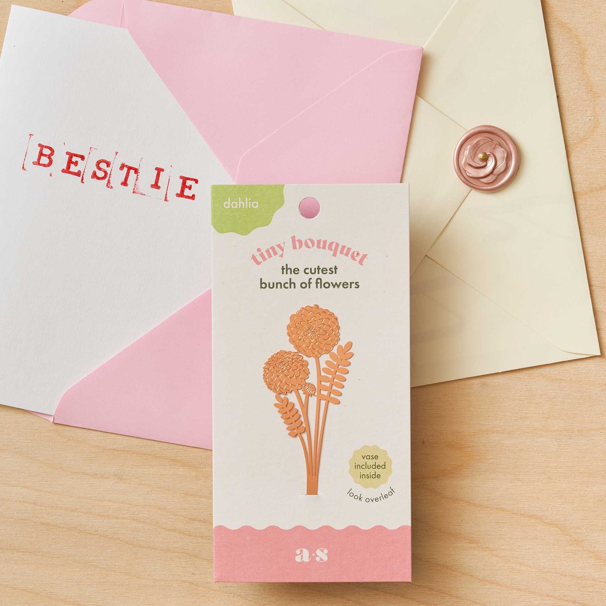 Floral-themed card with 'BESTIE' envelope and decorative elements on a wooden surface