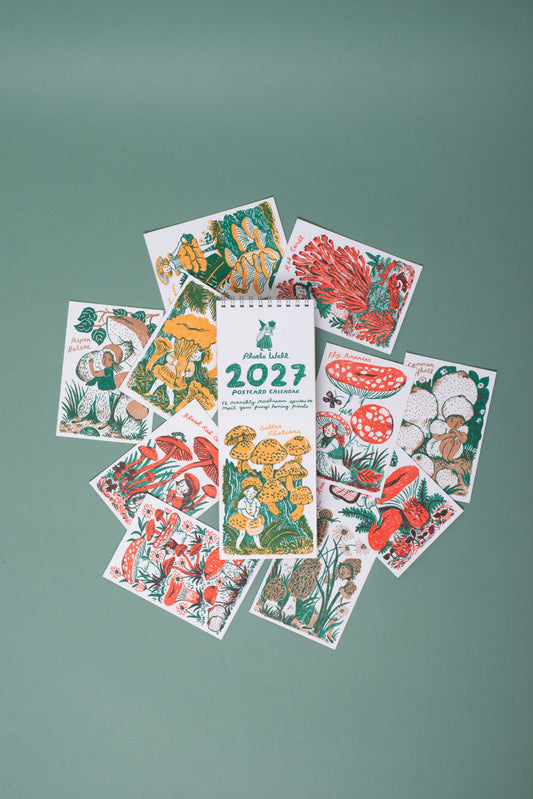 A spiral-bound 2027 mushroom-themed calendar or booklet lies centered on a muted green background, surrounded by several illustrated sample pages showing red, yellow, green, and brown botanical and mushroom drawings.