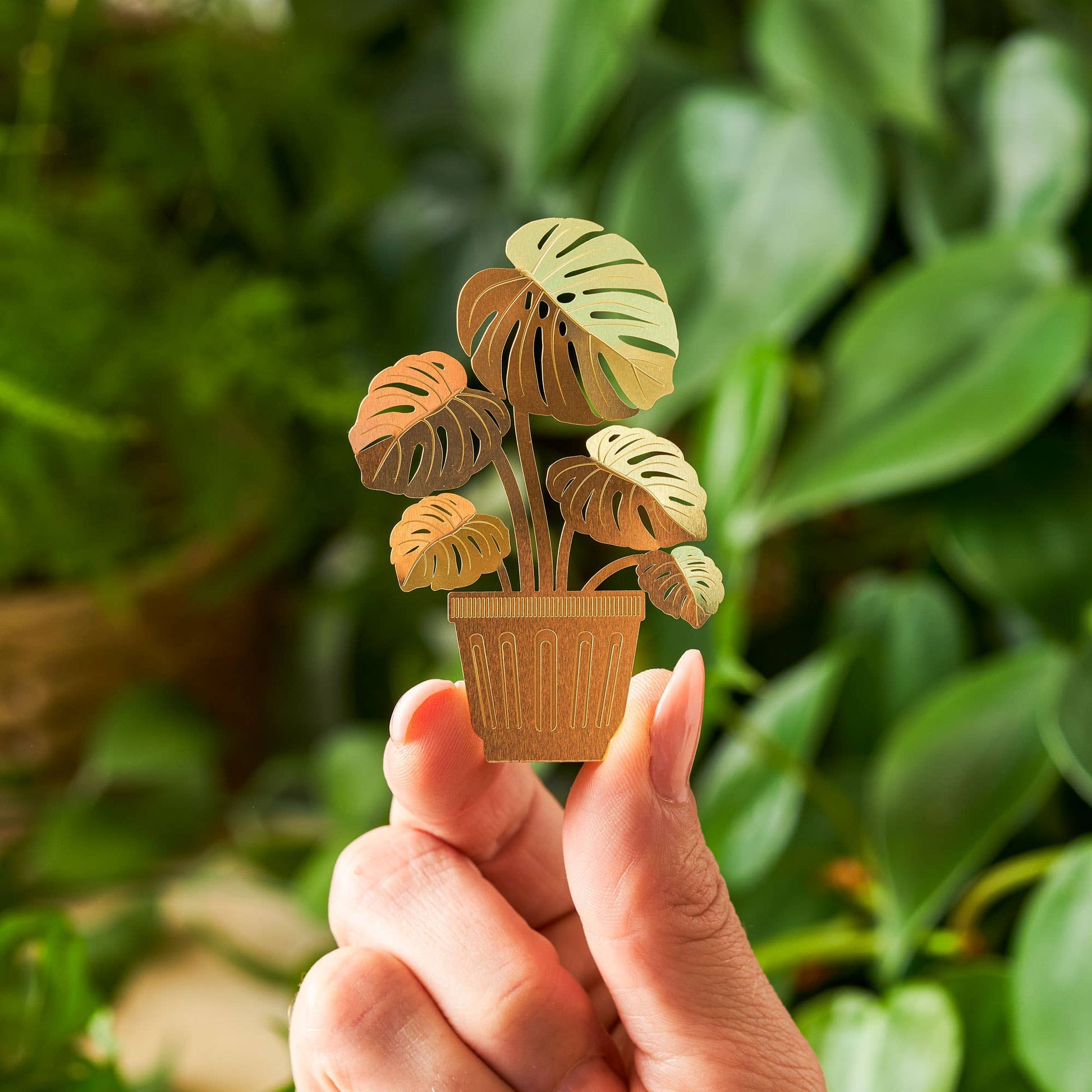 Hand holding a small wooden plant ornament against a green leafy background