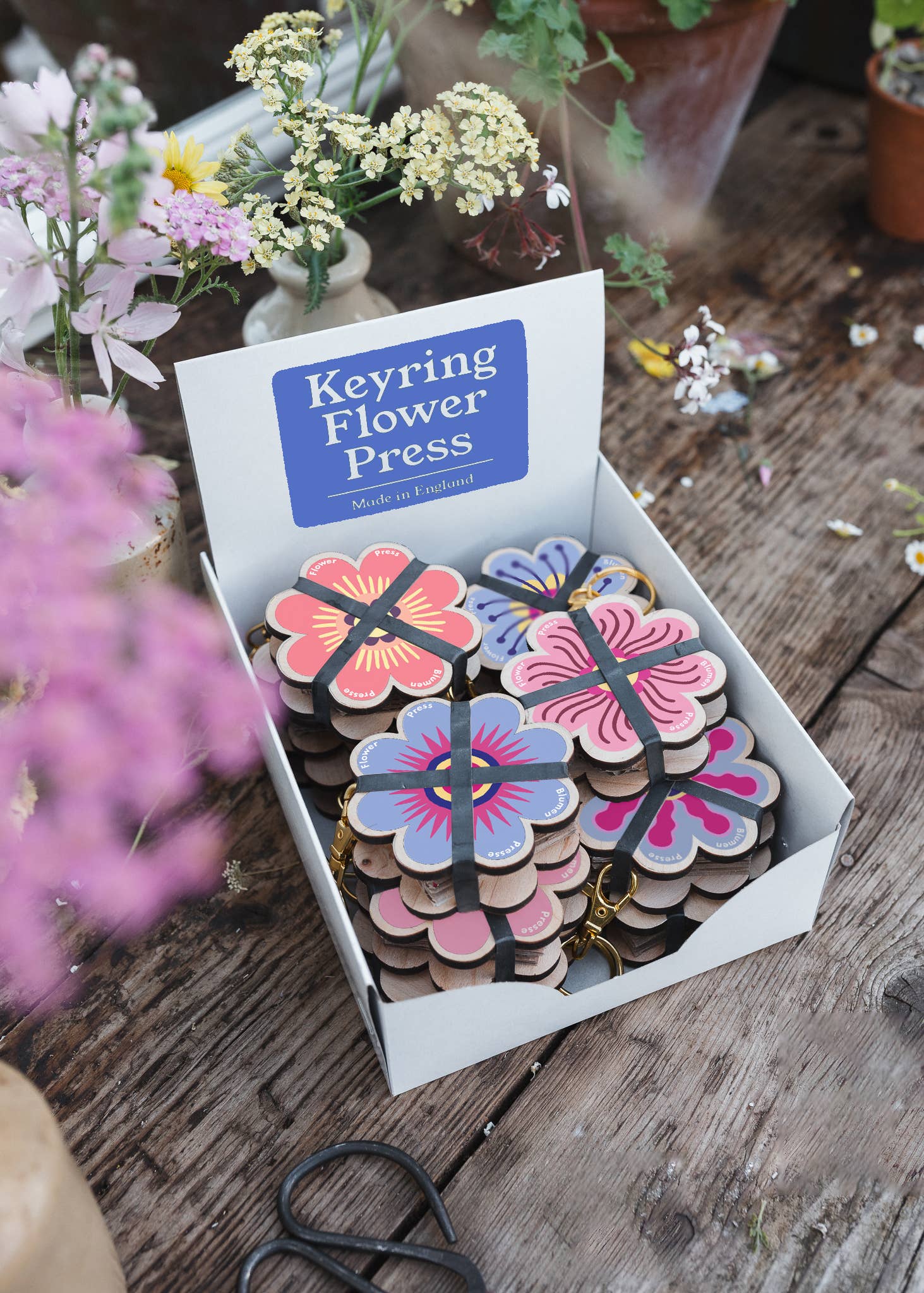 Keyring flower press in a box on a wooden surface with flowers around