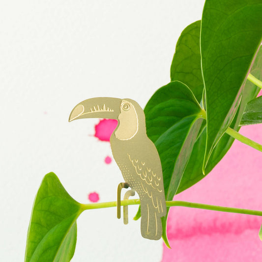 Gold toucan bird figurine on a branch with pink flowers and green leaves