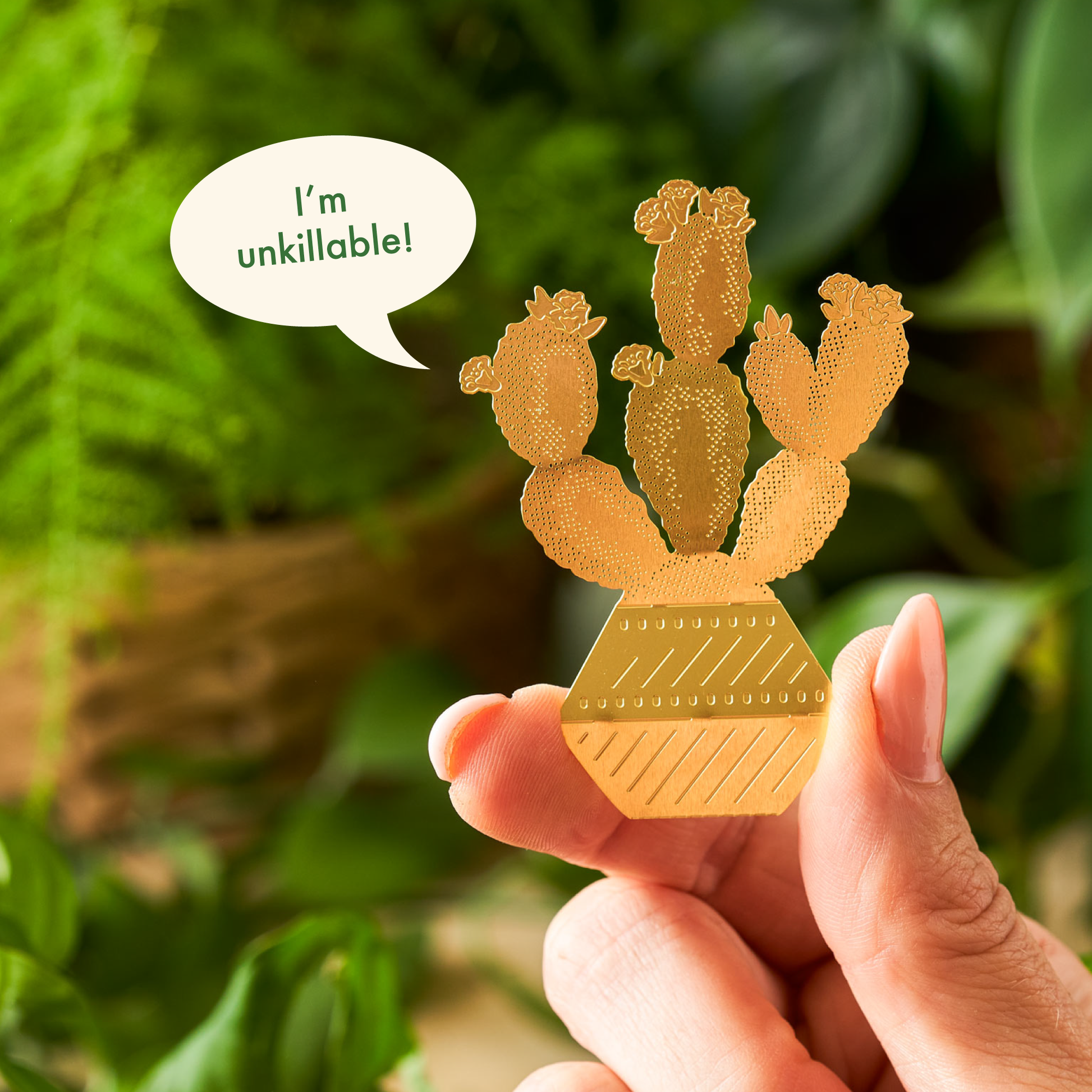 Gold cactus-shaped ornament held by a hand with a green leafy background