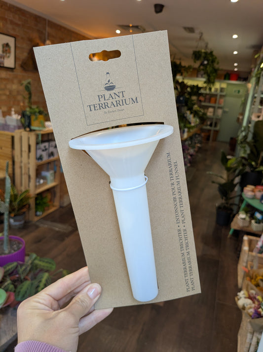 White terrarium tool on a brown card with 'Plant Terrarium' branding, held in a store setting.