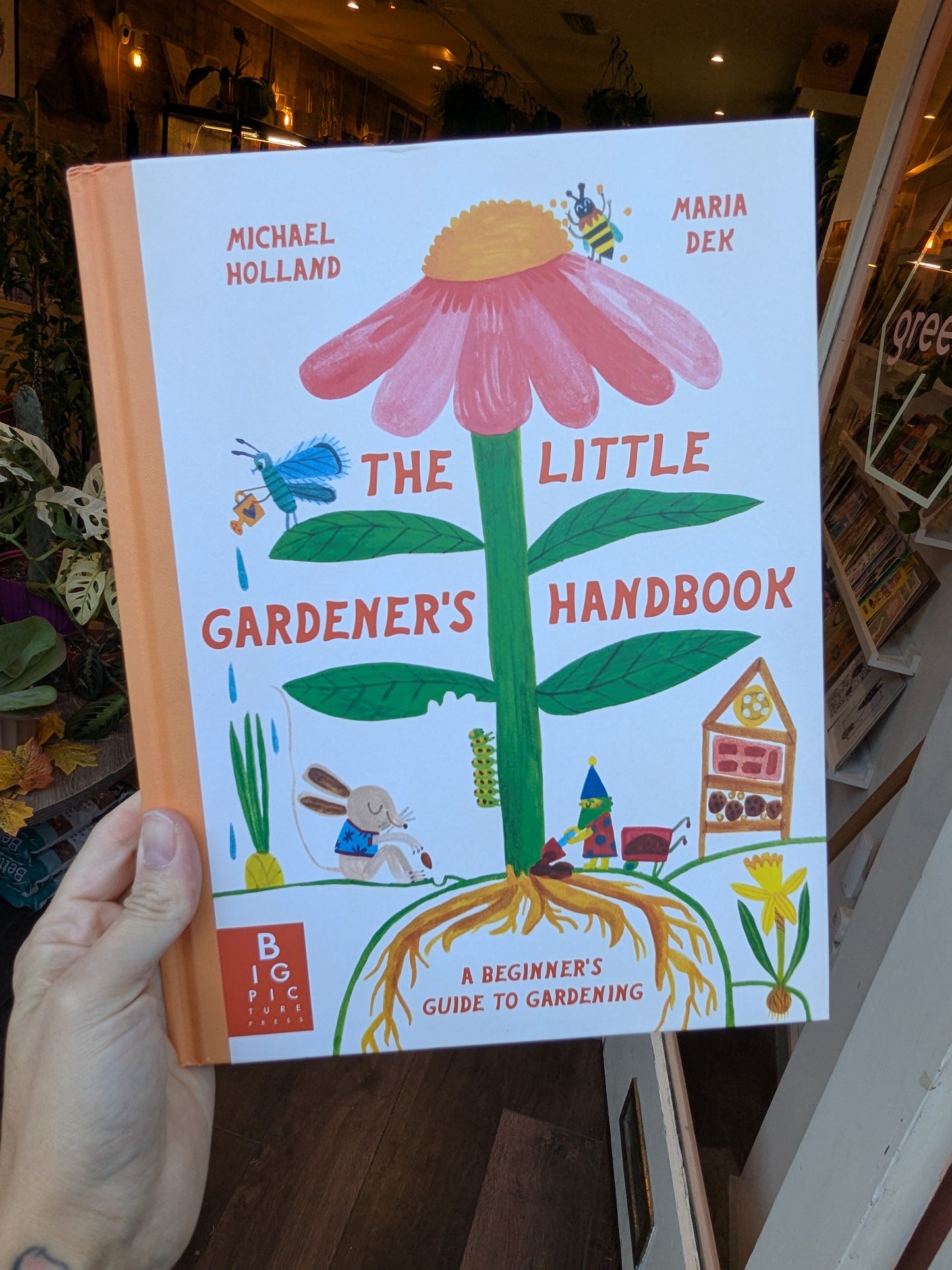 Book titled 'The Little Gardener's Handbook' held by a person indoors.