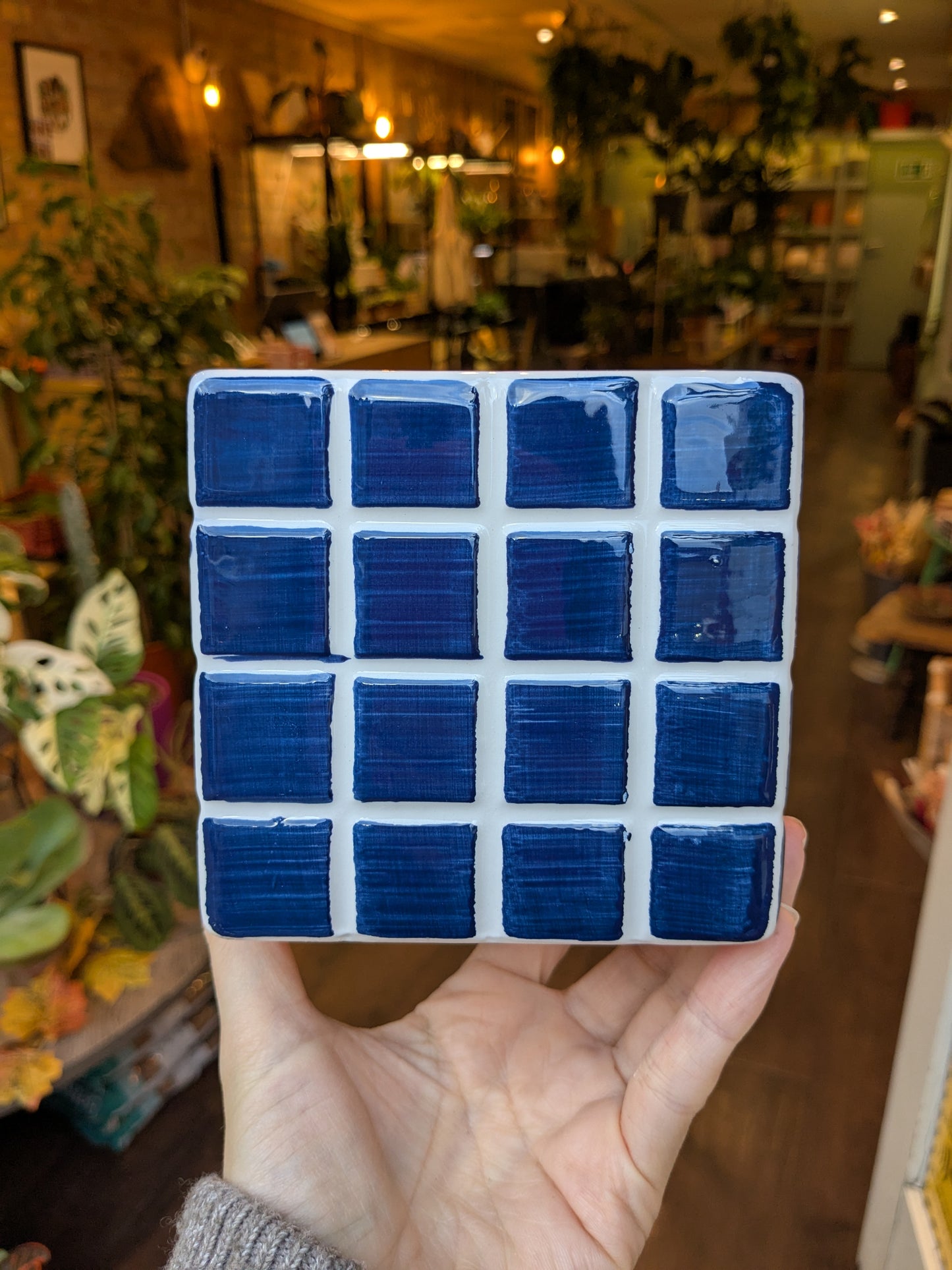 Hand holding a square of blue ceramic tiles in a store setting