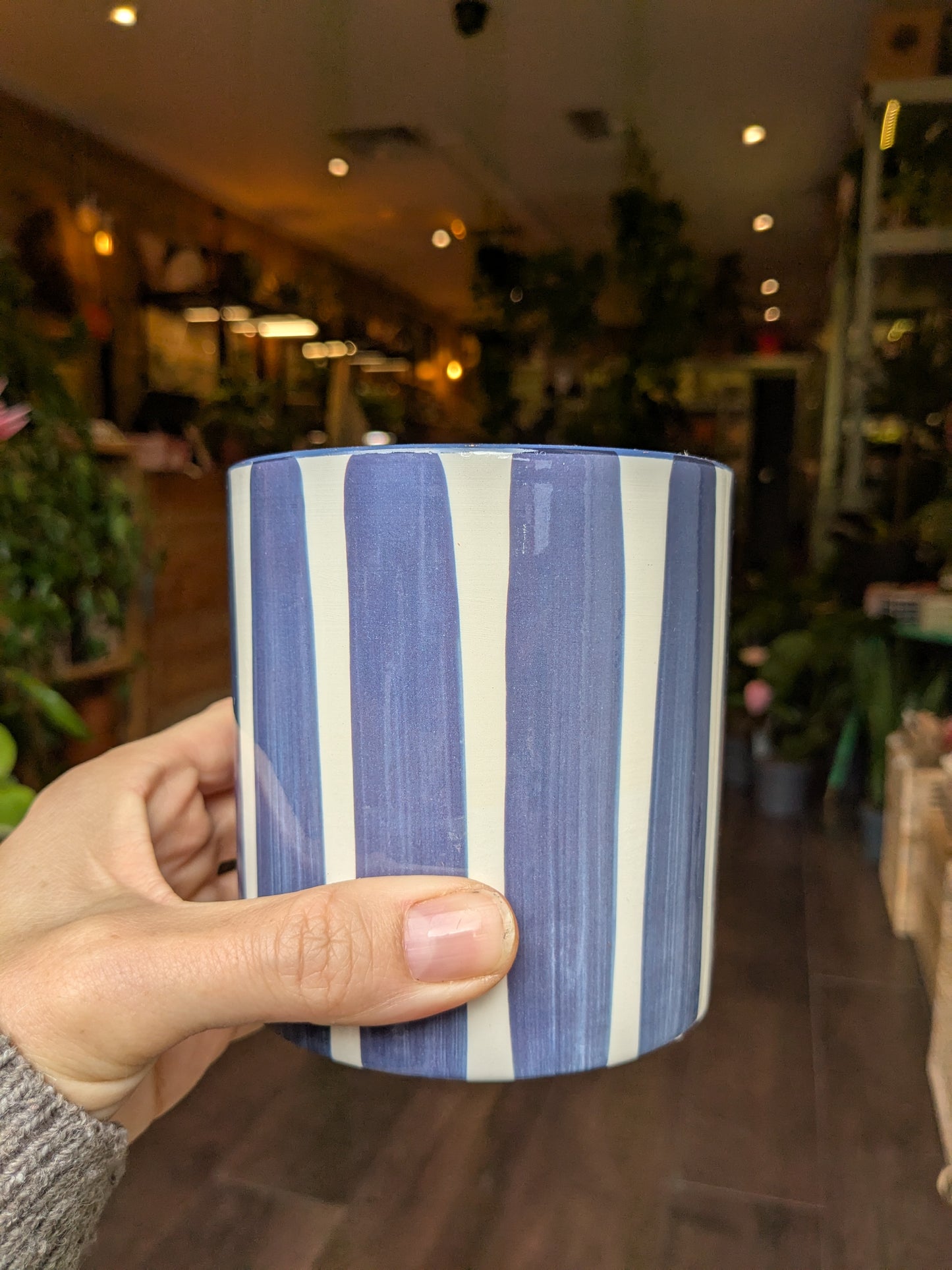 Blue and white striped mug held in a hand with a blurred indoor background