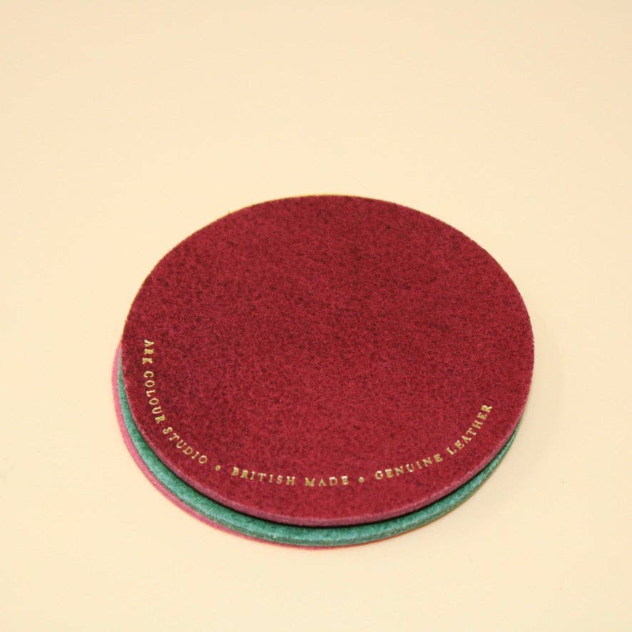 Two round red leather coasters with text on a beige background