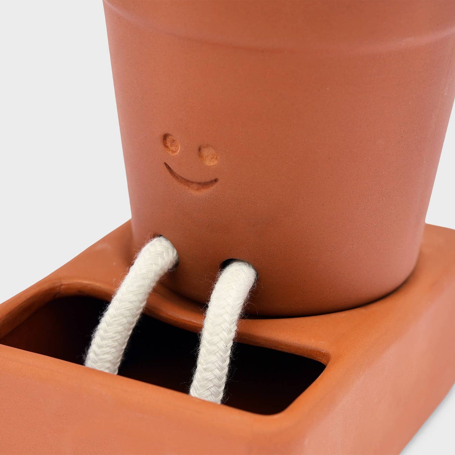 Terracotta pot with a face and white strings hanging out, placed inside a larger terracotta container.