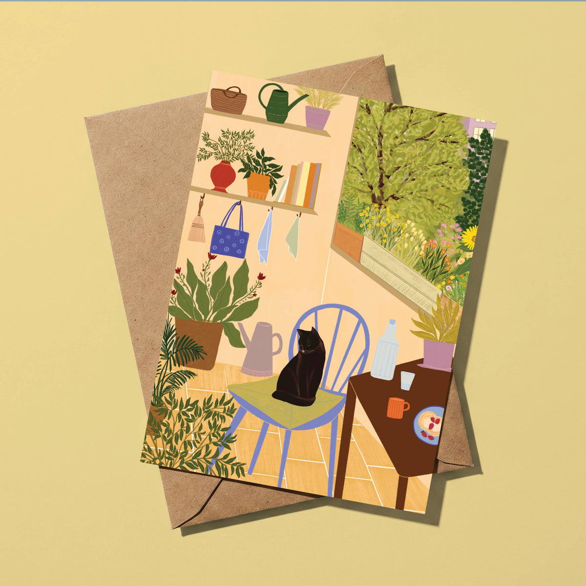 A rectangular illustrated card or print with a whimsical indoor garden scene and a black cat sitting on a chair, layered over a brown kraft envelope on a pale yellow background.